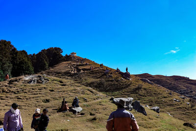 Rear view of people walking on land against clear blue sky