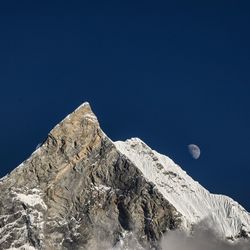 Low angle view of snowcapped mountains against clear blue sky