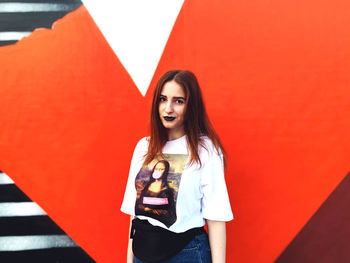 Portrait of smiling young woman standing against red wall