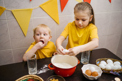 Girl breaks an egg into dough, brother helps cook, easter holiday