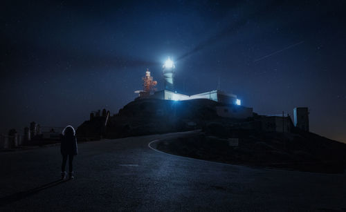 Rear view of man standing on illuminated building against sky at night