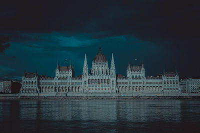 City at waterfront against cloudy sky at night