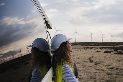 Engineer wearing hardhat leaning on van at wind farm