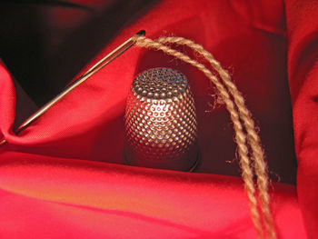 Close-up of needle by thimble on red fabric