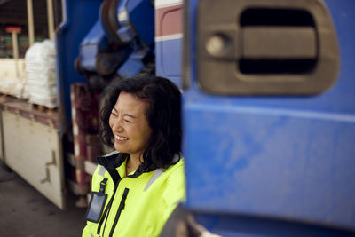 Happy mature female worker standing by truck at industry