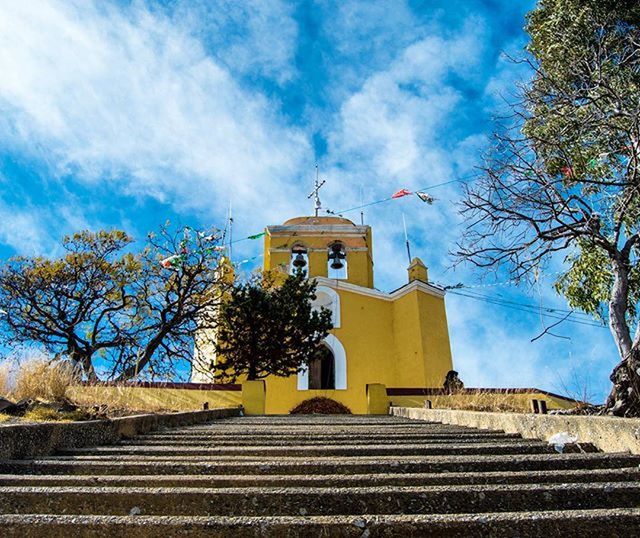 architecture, building exterior, built structure, church, religion, place of worship, sky, spirituality, tree, low angle view, house, cloud - sky, cross, roof, blue, cloud, day, outdoors