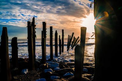 Wooden posts on beach against sky during sunset