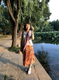 Portrait of woman standing on footpath by lake