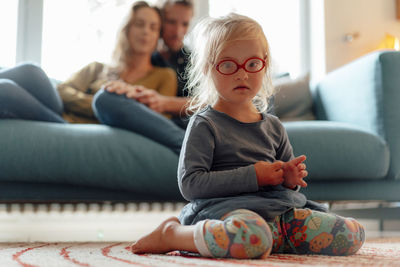 Cute little blond girl wearing eyeglasses sitting in living room at home