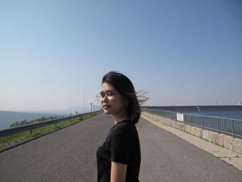 Portrait of young woman standing on road against clear sky