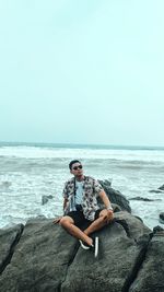 Man sitting on rock by sea against sky