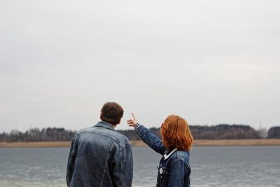 Rear view of couple standing by lake against sky