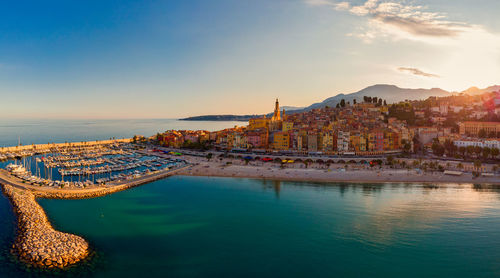 Buildings by sea against sky during sunset in city