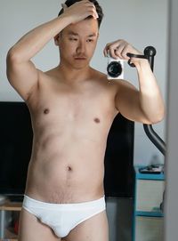 Reflection of shirtless man photographing while standing at gym in mirror