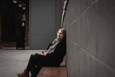 Side view full length portrait of woman sitting by wall