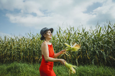 Woman wearing hat and red dress juggling corns walking at field