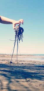 Man holding umbrella on beach against clear sky