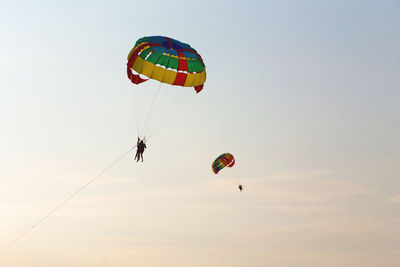 Low angle view of people parasailing against sky