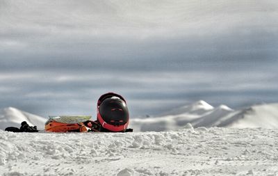 Skiing helmet and bag on snowcapped mountain against cloudy sky