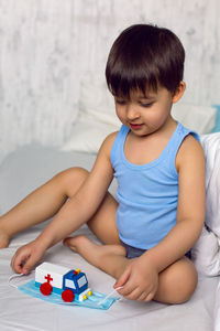 Child plays with a wooden ambulance toy on the bed