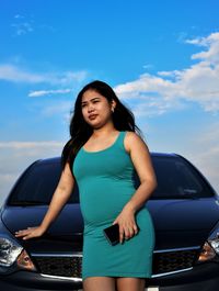 Beautiful young woman standing by car against blue sky