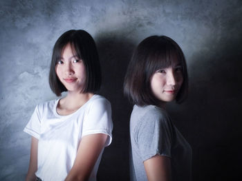 Portrait of smiling young sisters against gray wall