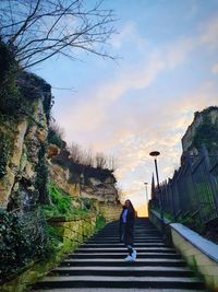 Rear view of woman walking on staircase against sky