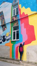 Full length rear view of woman painting on building wall