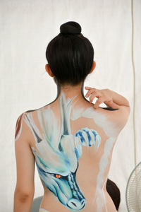 Rear view of shirtless woman with painted back standing against wall