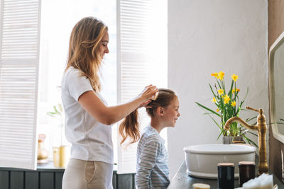 Young mother with little tween girl in pajamas combs her hair on morning in bathroom at home