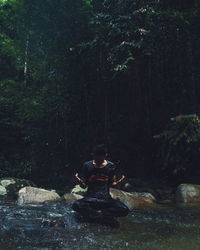 Young man sitting in rock in stream at forest