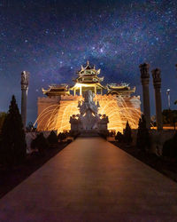 Illuminated building and statue against sky at night