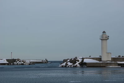 Lighthouse by sea against clear sky