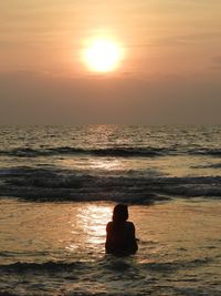 Silhouette people sitting on sea against sky during sunset