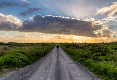 Man standing on road amidst landscape against sky during sunset