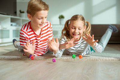 Cheerful siblings playing with dice while lying on carpet at home