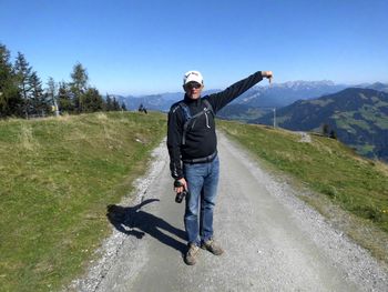 Portrait of mature man with camera gesturing while standing on mountain road 