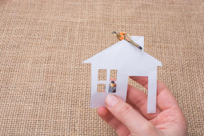 Cropped hand holding paper house with figurines over burlap