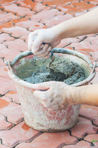 Cropped hands of man mixing cement in bucket on floor