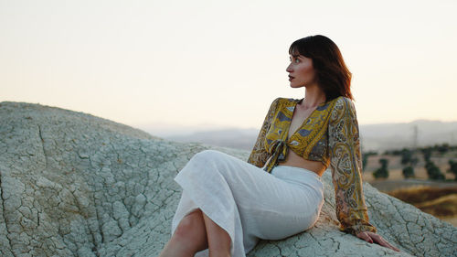 Beautiful girl observes the sunset sitting in the mountains on the rock