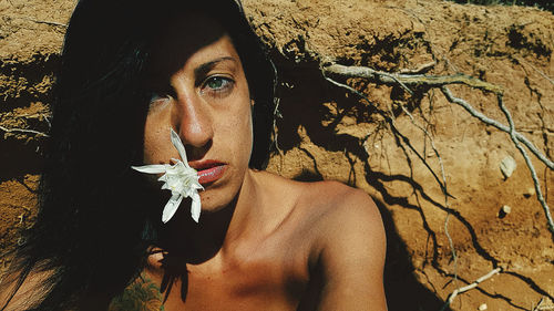 Portrait of shirtless woman with white flower in mouth at beach