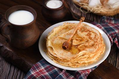 Homemade thin pancakes with honey stacked in a stack, on a wooden table with a mug of milk, 