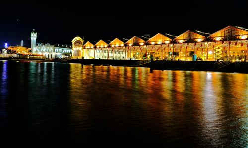 Illuminated buildings by river against sky at night