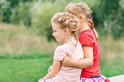 Two girls toddler sisters sit hugging on the bridge in the park. support.