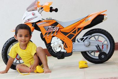Portrait of boy sitting against toy bike