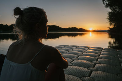 Rear view of woman looking at lake against sky during sunset