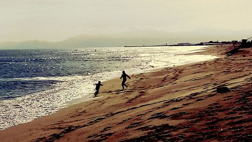 Silhouette men on beach against sky during sunset