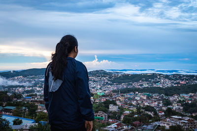 Young girl watching downtown city view with dramatic cloudy sky at evening from mountain top