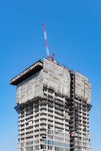 Low angle view of crane by building against clear blue sky