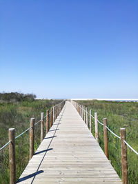 View of wooden bridge against clear blue sky